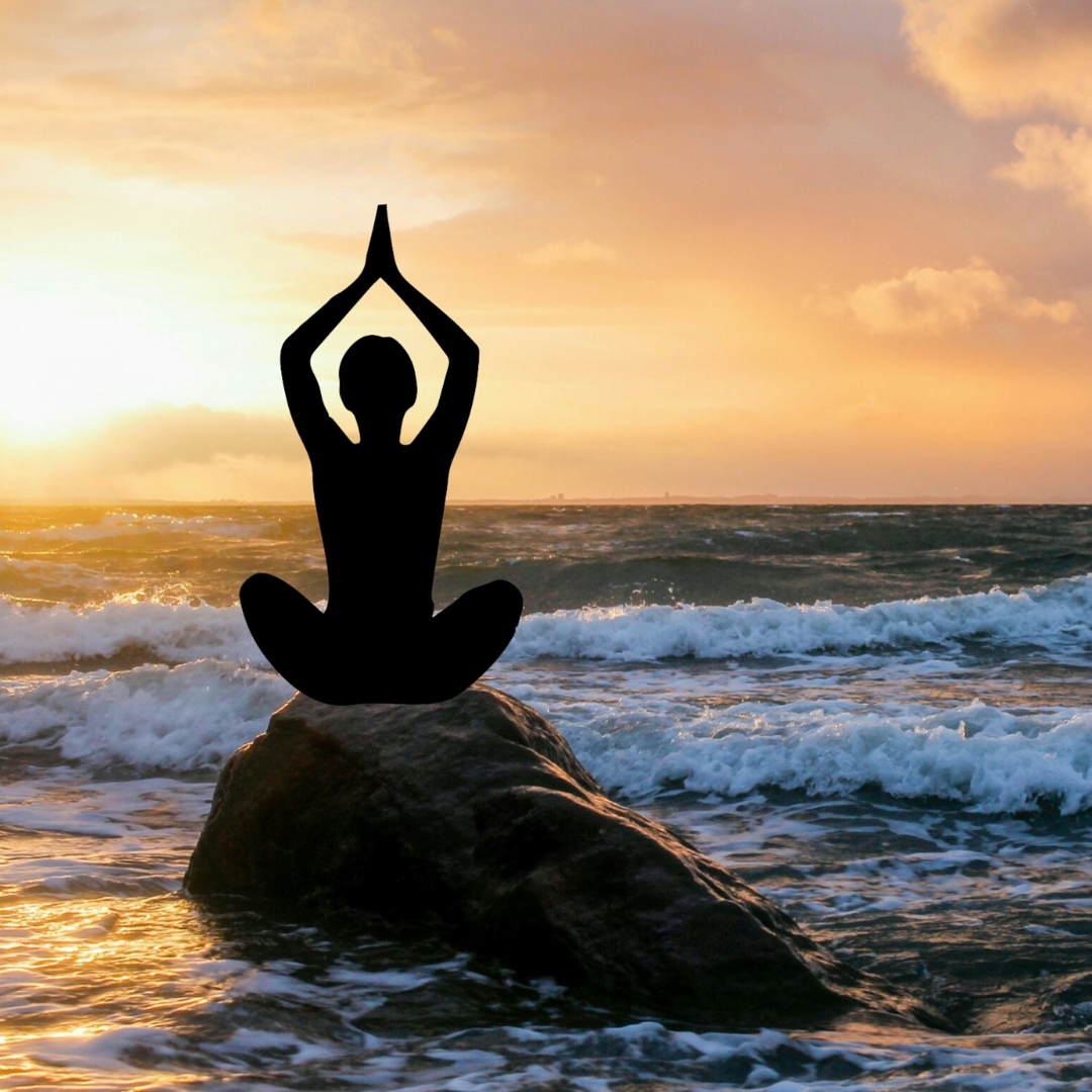 Silhouette of meditator on a rock on the beach with waves and glow from the sun