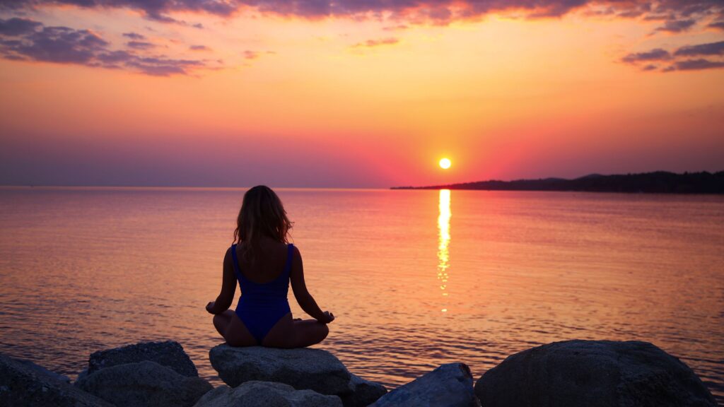 silhouette of woman sitting meditating on the beach at sunset