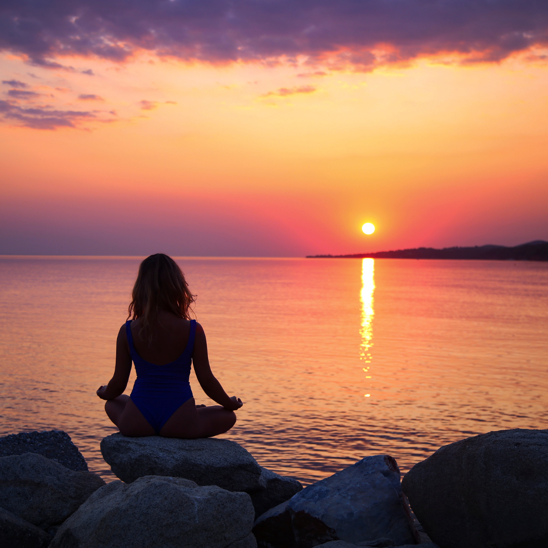 woman sitting in stillness on the water watching a sunset