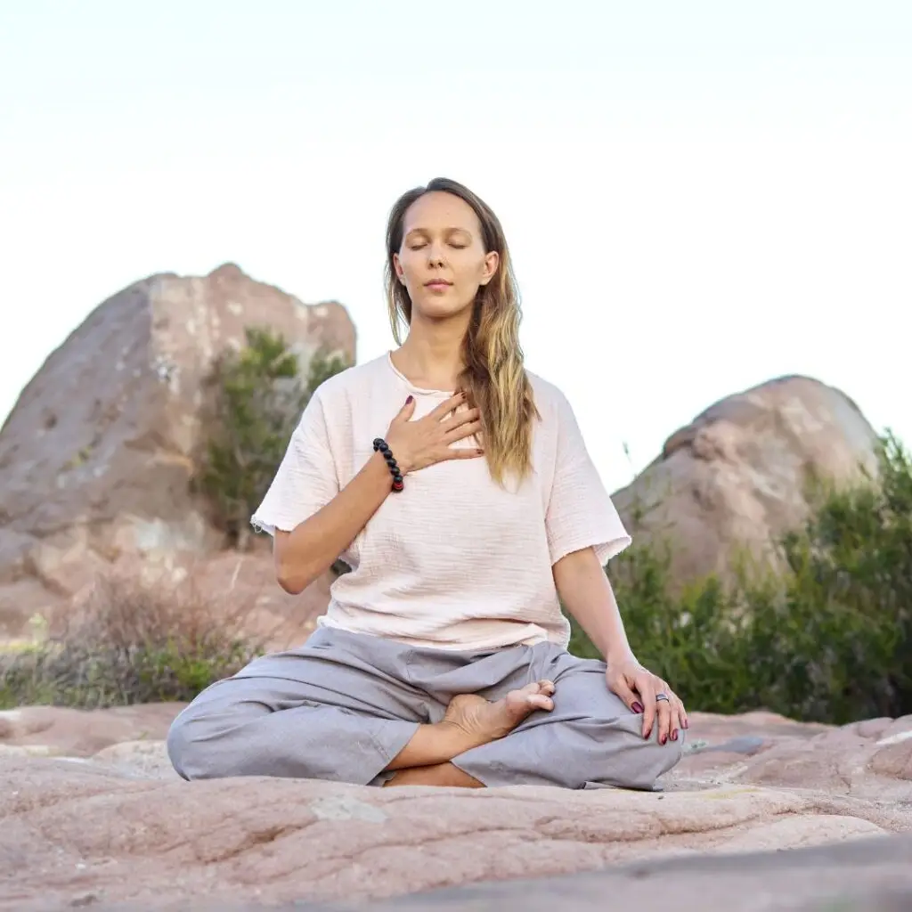 woman meditating on beach with a hand on her heart