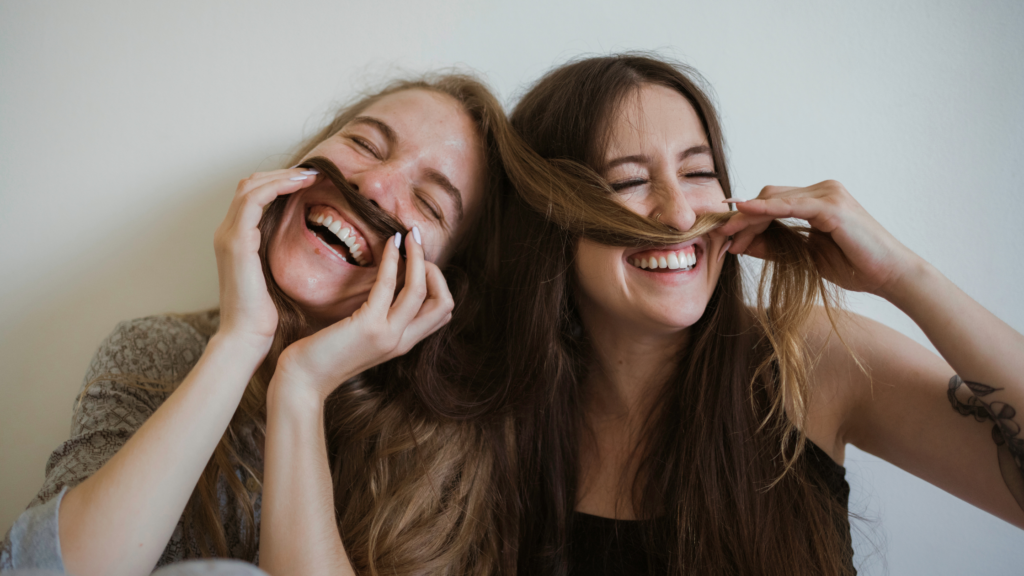 two women laughing and using each other's hair as mustaches